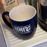 Picture of the navy blue/white WMPG mug on a coffee tray next to a kettle.