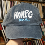 Picture of a hand holding this gray hat with the WMPG logo in white on the front.