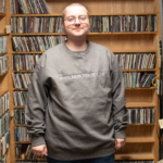 Picture of a WMPG member wearing a gray crewneck with white embroidered letters reading "WMPG: Break Through the Static"
