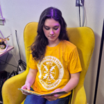 Picture of a WMPG member modeling a yellow t-shirt on a yellow chair.