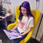 Picture of WMPG member wearing a white t-shirt with red design while holding a vinyl record.