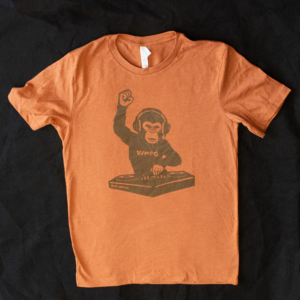 Picture of orange t-shirt with a design of a DJ monkey in gray on it on a black background.