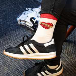 Picture of a WMPG member wearing a cream color sock with red accents. The design on the ankle is a heart with the line "WMPG has my heart" on it.