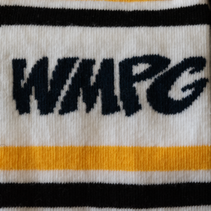 Picture of a close-up of the logo on the WMPG yellow and black socks. The logo is black text on a white sock. Above and below the logo are black and yellow stripes.