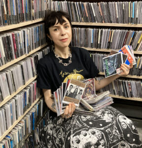 Justine Henry, volunteer Music Director, poses in the music library with piles of CDs.